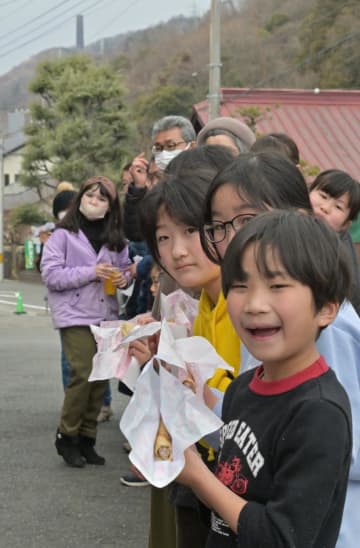 大煙突(奥左)を背に「桜ソーセージたらし焼き」を食べる参加者=日立市白銀町