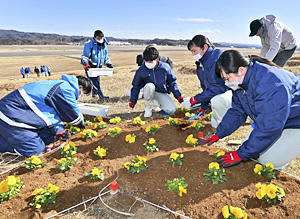 空港滑走路の西側斜面に、記念文字の花植えをする生徒や関係者＝20日午後