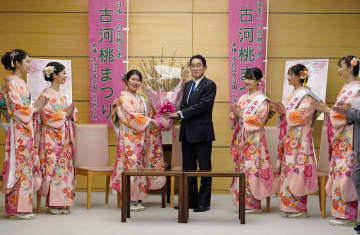 「古河桃むすめ」の田中佑佳さん(左から3人目)から桃の花束を贈られる岸田首相=24日午前、首相官邸