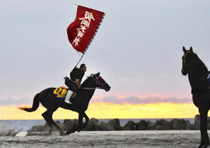 日の出を迎えた早朝の浜辺で、旗をなびかせながら乗馬訓練する騎馬武者＝南相馬市鹿島区・烏崎海岸（坪倉淳子撮影）