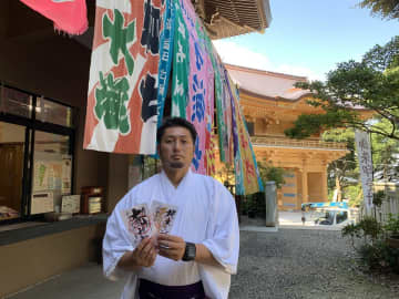 (上)神門(右後ろ)完成を祝う大漁旗で装飾された大甕神社儀式殿の社務所前で禰宜の朝日正敬さん=日立市大みか町、例大祭後に大漁旗は撤去(下)大甕神社の御朱印。左が「大甕神社」版、右は「甕星香々背男」版