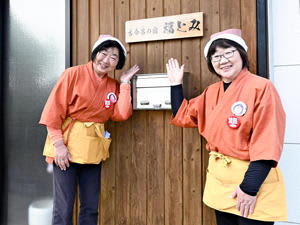 「お父さんも喜んでくれているかな」と看板の前で笑顔を見せる渡辺さん（左）