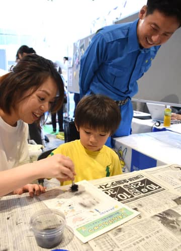 指紋採取体験で、粉末を振りかけて指紋を浮かび上がらせる参加者＝25日、クイーンズスクエア横浜