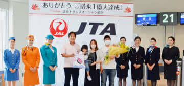 乗客を代表して花束が贈られた小倉陽子さん（中央）とJTAの野口望社長（左から4人目）ら関係者＝15日、那覇空港