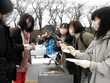 串に刺したアユの焼き具合を確かめる参加者ら＝14日午前、厚木市の厚木青少年広場